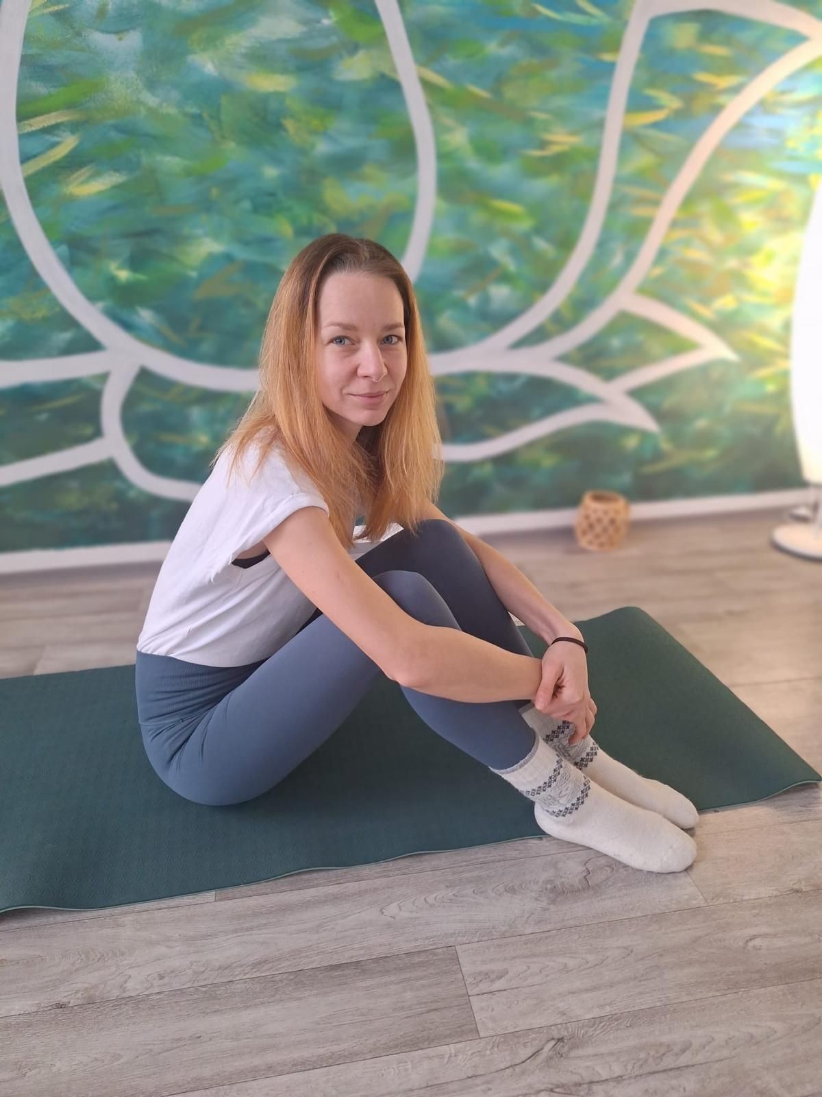 Woman sitting on a yoga mat indoors with abstract wall art background.