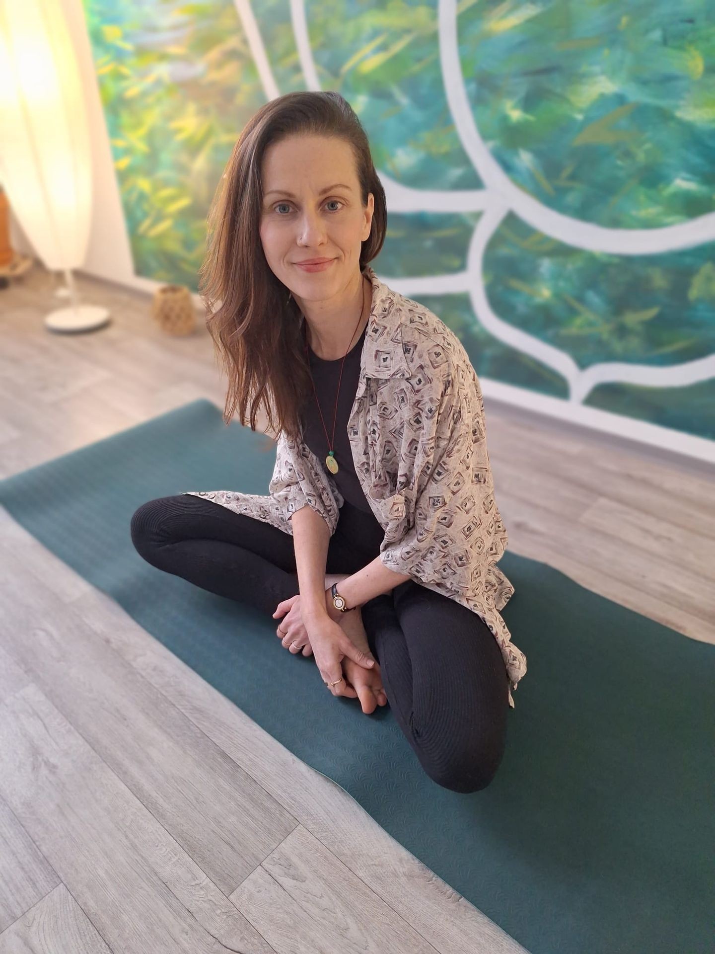 Person sitting cross-legged on a yoga mat indoors with a colorful abstract wall background.